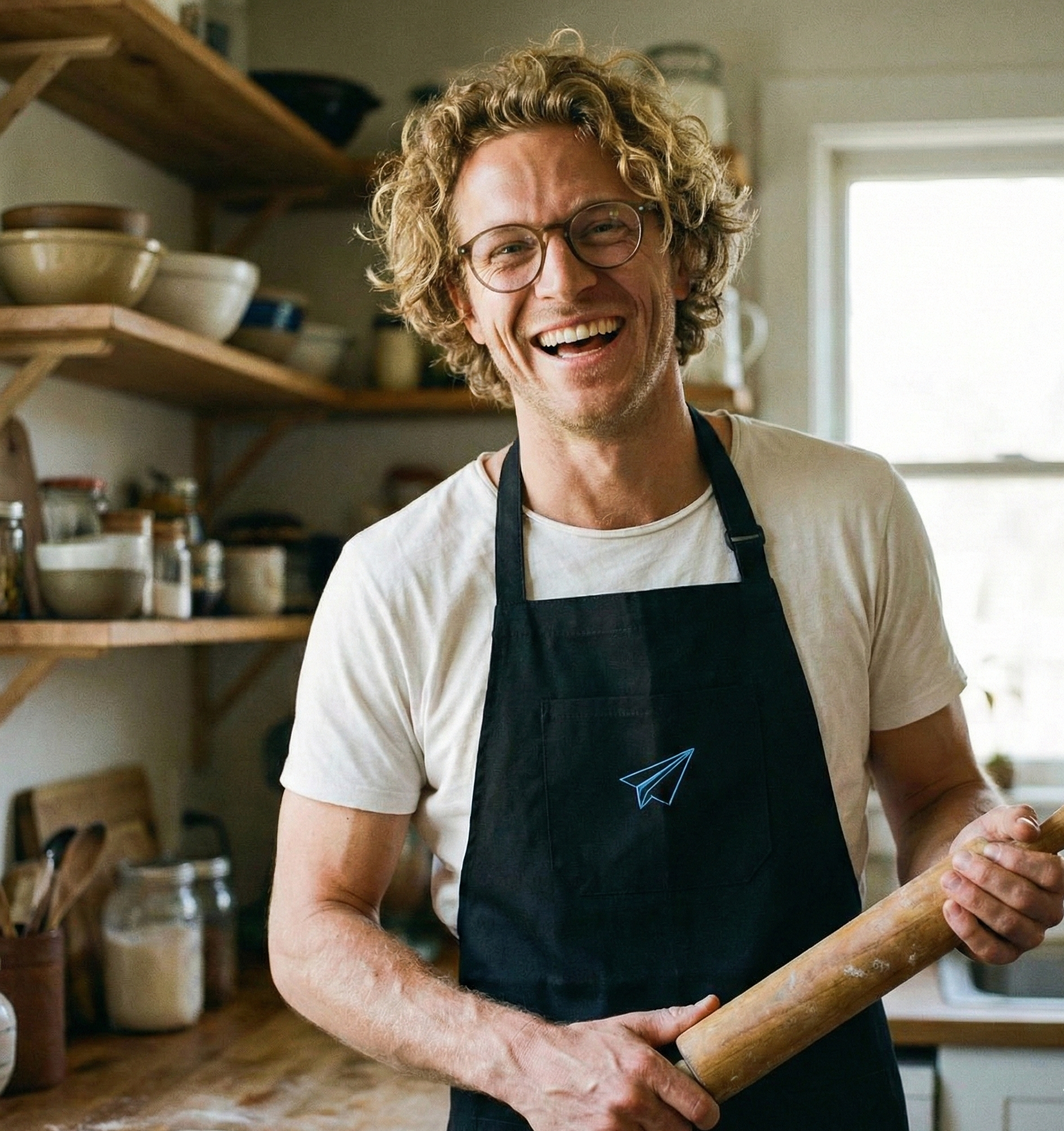 homme souriant dans une cuisine tenant un rouleau à patisserie et portant un tablier de cuisine célébrant les noces de papier