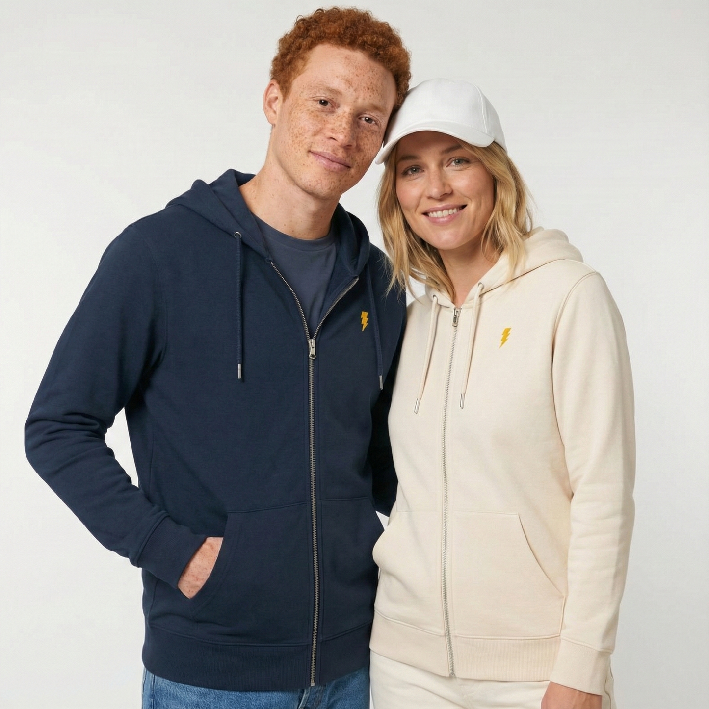 un homme et une femme portent un hoodie zippé unisexe floqué avec un logo représentant les noces d'électricité
