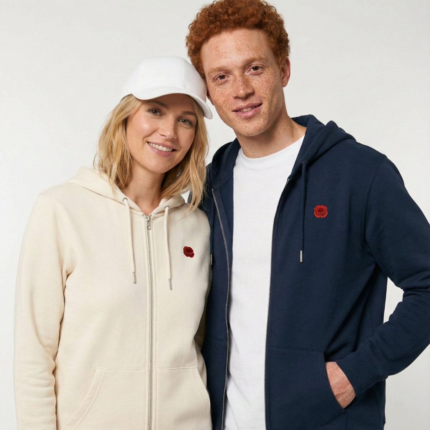 un homme et une femme portent un hoodie zippé unisexe floqué avec un logo représentant les noces de coquelicot