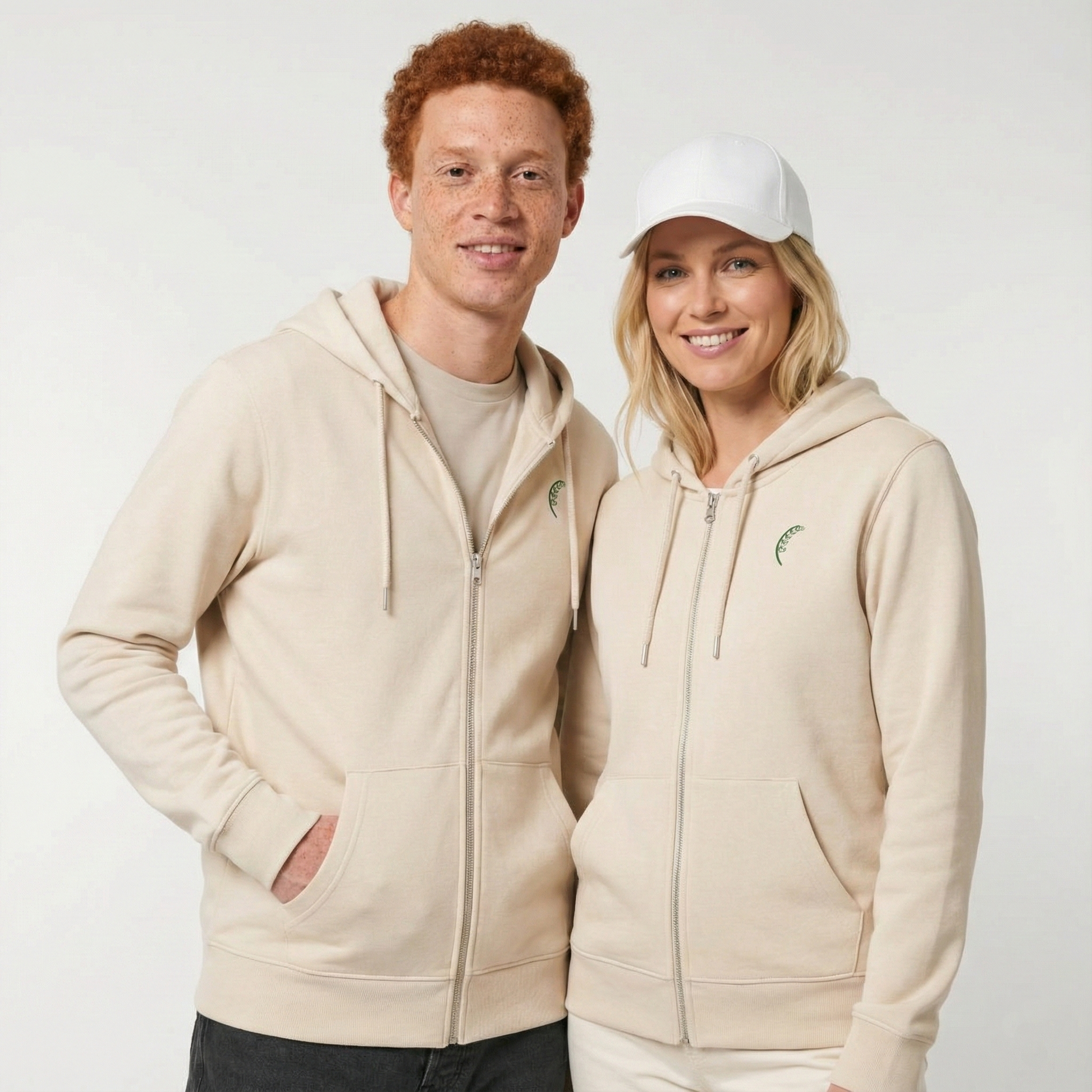 un homme et une femme portent un hoodie zippé unisexe floqué avec un logo représentant les noces de muguet